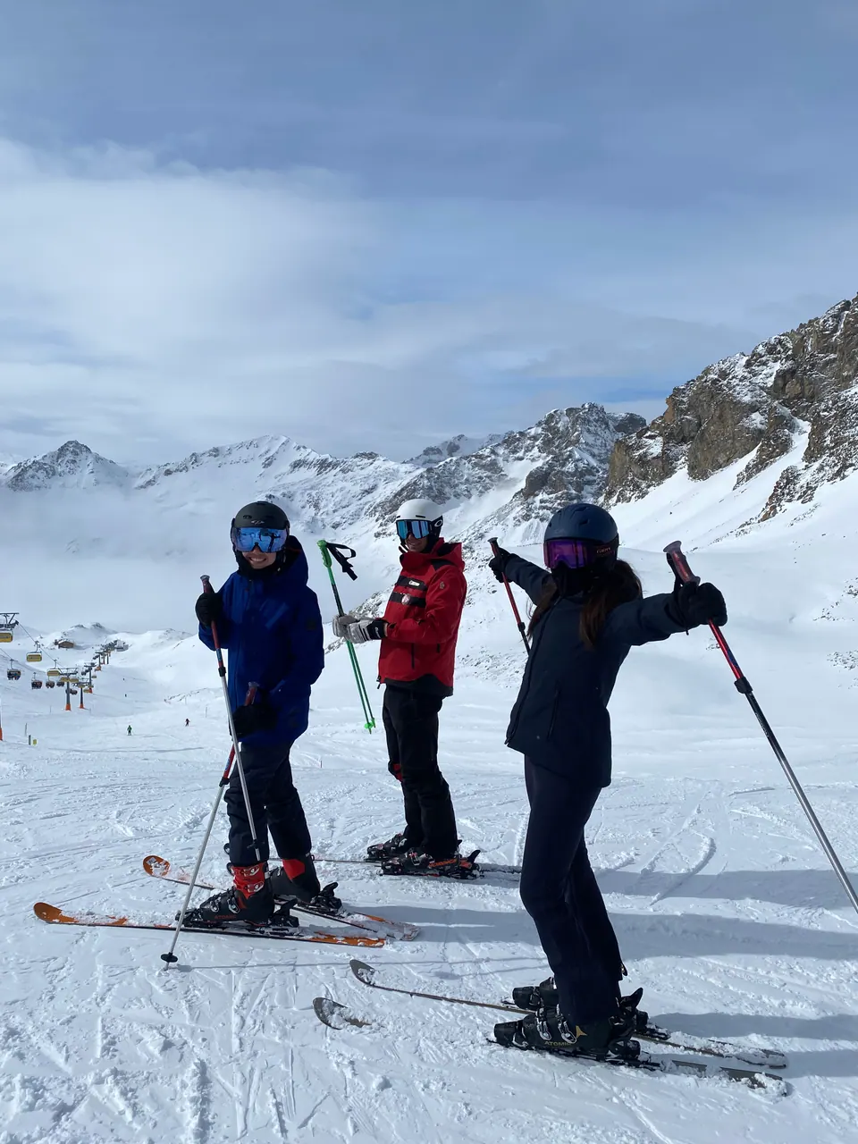Three skiers in helmets and goggles on a snowy slope with mountains behind